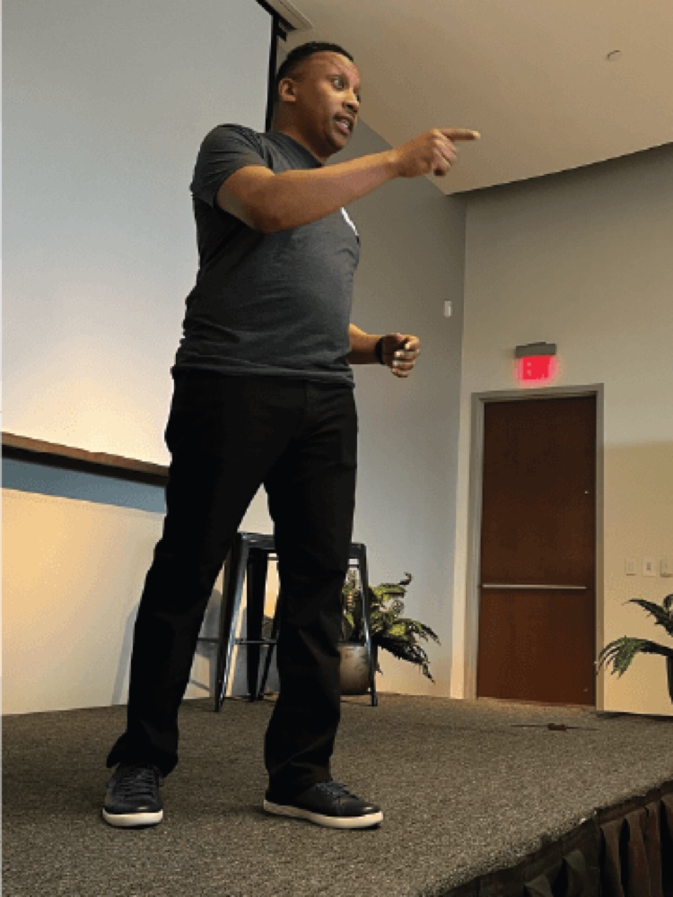 Mike Henry speaking on stage, pointing at the audience